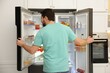 © New Africa - Man near open refrigerator with different food products in kitchen