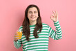 © New Africa - Happy woman with glass of juice showing okay gesture on pink background