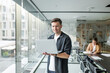 © muse studio - Man working on laptop in modern office space during the day with another person focused on paperwork in the background
