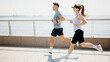 © muse studio - Two people run along a waterfront path on a sunny day near a city skyline with water in view