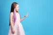 © New Africa - Cute girl with pink clip-in hair extensions looking in mirror on light blue background. Space for text
