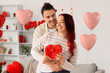 © Pixel-Shot - Young lovely couple with gift hugging at home. Valentine's Day celebration
