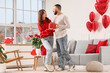 © Pixel-Shot - Young man greeting his girlfriend with heart-shaped gift at home. Valentine's Day celebration