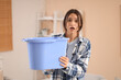 © Pixel-Shot - Shocked young woman placing blue bucket under water dripping from ceiling at home