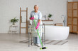 © Pixel-Shot - Mature woman with walker and broom sweeping floor in bathroom