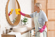 © Pixel-Shot - Mature woman with walker and rag cleaning mirror in bathroom