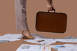 © Pixel-Shot - Leg of woman in high heels with many newspapers and suitcase on brown background, closeup