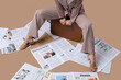 © Pixel-Shot - Young woman in high heels with many newspapers sitting on suitcase against brown background, closeup