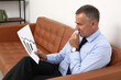 © Pixel-Shot - Worried mature businessman with business graphic biting nails on sofa in office