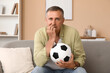 © Pixel-Shot - Worried mature man with soccer ball biting nails while watching TV at home