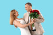 © Pixel-Shot - Happy mature couple with bouquet of roses dancing on blue background. Valentine's Day celebration