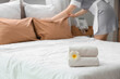 © Pixel-Shot - Young female chambermaid with clean towels and plumeria flower making bed in hotel room, closeup