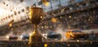 © Bi - A golden trophy sits in the foreground of a race track with cars and confetti