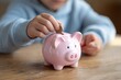 © Fadhel - Close-up of a child's hand placing a coin into a pink piggy bank