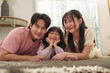 © eggeeggjiew - Happy Asian family portrait with parents and daughter smiling while lying on the carpet, warm and relaxed home.