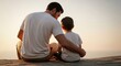 © Liam - Father and son sitting embracing on a rock watching the golden sunset vista. Symbolizing connection, protection, and quality family time.