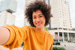 © Jose Calsina - A happy young woman taking a cheerful selfie while smiling brightly, showcasing her joyful personality and enthusiasm for life in a dynamic urban location filled with energy and excitement.