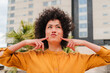 © Jose Calsina - A cheerful young woman with curly hair playfully posing and making funny faces while smiling joyfully, radiating happiness and confidence in a delightful and engaging manner that captures attention.