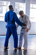© wavebreak3 - Diverse male training partners grappling on padded mats in dojo with gis, belts and windows