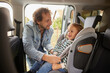 © Stockphotodirectors - A dad is securing his young daughter in her car seat in the back of their vehicle. He is smiling at her while adjusting her safety harness. She is also smiling and seems excited.