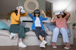 © wavebreak3 - Diverse female friends wearing VR headsets and reacting on light gray couch in living room