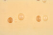 © nahhan - Close up top view of a smooth yellow swiss cheese surface featuring characteristic round holes and a creamy texture