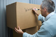 © DragonImages - Middle aged Caucasian man labeling large cardboard box with marker, writing word Winter on surface while organizing or preparing items for storage in self storage facility