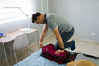 © AntonioDiaz - Adult Hispanic man struggling to close an overstuffed luggage, packing clothes for an upcoming trip in the bedroom