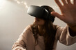 © Westend61 - Young woman using VR headsets playing games on the sofa at home at night