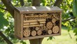 © DisignUA - Wooden insect hotel hanging on a tree branch with a bee resting on the bamboo tubes in summer.
