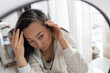 © Mykola - Middle aged Asian woman looks in the mirror at her gray hair roots. Problem of gray hair and loss hair.