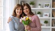 © Vasiliy - Mature mother and adult daughter smiling with a bouquet of tulips. Two women hugging in a bright living room. Mother's Day celebration concept