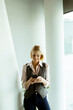 © BGStock72 - Woman using smartphone while leaning against a modern wall in a bright indoor space