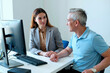 © Mediaphotos - Young woman sitting at desk talking with adult man in office setting, both looking at each other, computer monitor and keyboard on desk