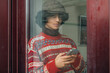 © tetxu - Young man looking out the window on a cold, rainy day while using his mobile phone