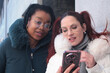 © tetxu - Woman showing her mobile phone to her friend on the street on a winter day
