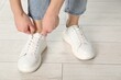 © New Africa - Woman tying shoelace of white sneaker indoors, closeup