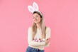 © New Africa - Easter celebration. Portrait of smiling woman in headband with bunny ears holding painted eggs on pink background
