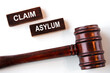 © Zhanna - CLAIM ASYLUM - words on wooden brown bars on a white background with a judge's gavel