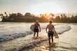 © Soloviova Liudmyla - Father with teenager son walking with surfboards by the sandy ocean beach with palm trees on background lightened with sunset sun. They smiling and have a conversation. Family active vacation concept