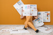 © Pixel-Shot - Young woman in high heels with many newspapers sitting on floor near orange wall