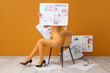 © Pixel-Shot - Young woman in high heels with many newspapers sitting on chair near orange wall