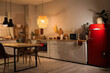 © Pixel-Shot - Interior of modern kitchen with glowing lamps, white counter, refrigerator and laptop on dining table at evening