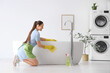 © Pixel-Shot - Beautiful young happy woman with bottle of detergent and rag cleaning bathtub in bathroom