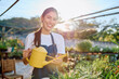 © we.bond.creations - Young woman smiling, holding yellow watering can, caring for plants in a sunny garden center. Green thumb enjoying horticulture