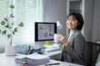 © Wasana - Young office worker drinking coffee and smiling while working on a desktop computer