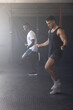 © wavebreak3 - Diverse male friends in sportswear skipping jump ropes on rubber mat in gym beside squat rack