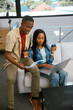 © wavebreak3 - African American coworkers sitting on gray sofa in home office collaborating on laptop with coffee