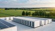 © Johnnii - A modern solar energy facility featuring large battery storage units, surrounded by lush green fields under a clear sky.