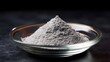 © Bussakon - A pile of fine grey chemical powder in a clear glass dish on a dark textured surface